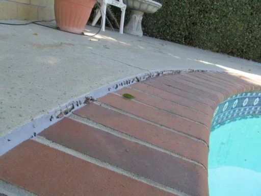 BEFORE A pool edge with a concrete surface and a few scattered leaves nearby.