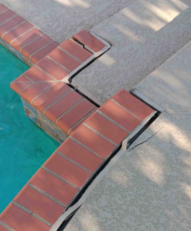 BEFORE Cracked pool deck tiles near the edge of a swimming pool.