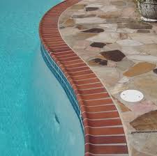 AFTER Curved stone patio surrounding a clear blue swimming pool.